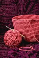 Ball of pink thread with a needle and knitted fabric on a background of purple material. Copy, empty space for text photo