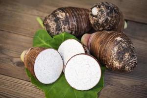 raíz de taro orgánica cruda fresca lista para cocinar, raíz de taro con media rebanada en hoja de taro y fondo de madera foto