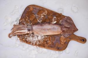calamares crudos sobre hielo con especias de ensalada lima limón en el fondo de la tabla de corte de madera, calamares frescos pulpo o sepia para comida cocinada en el restaurante o mercado de mariscos foto