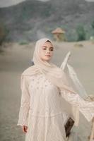 Beautiful islamic female model wearing hijab fashion, a modern wedding dress for muslim woman walks along the sand and the sea. A asian girl model using hijab having fun at the beach. Photo prewedding