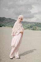 hermosa modelo femenina islámica con moda hijab, un vestido de novia moderno para mujeres musulmanas camina por la arena y el mar. una modelo asiática usando hijab divirtiéndose en la playa. foto preboda