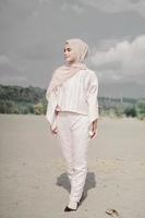 Beautiful islamic female model wearing hijab fashion, a modern wedding dress for muslim woman walks along the sand and the sea. A asian girl model using hijab having fun at the beach. Photo prewedding