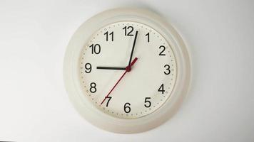 l'orologio da parete bianco indica l'ora. rotazione delle lancette corte e lunghe dell'orologio. sullo sfondo bianco. video