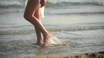 primer plano de las piernas de una mujer bailando en un agua de mar en una puesta de sol