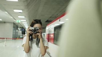 joven y hermosa turista asiática tomando fotos con una cámara de cine con un amigo, sonríe y disfruta en la plataforma de la estación de tren, feliz estilo de vida de viaje en viaje de vacaciones en transporte subterráneo. video