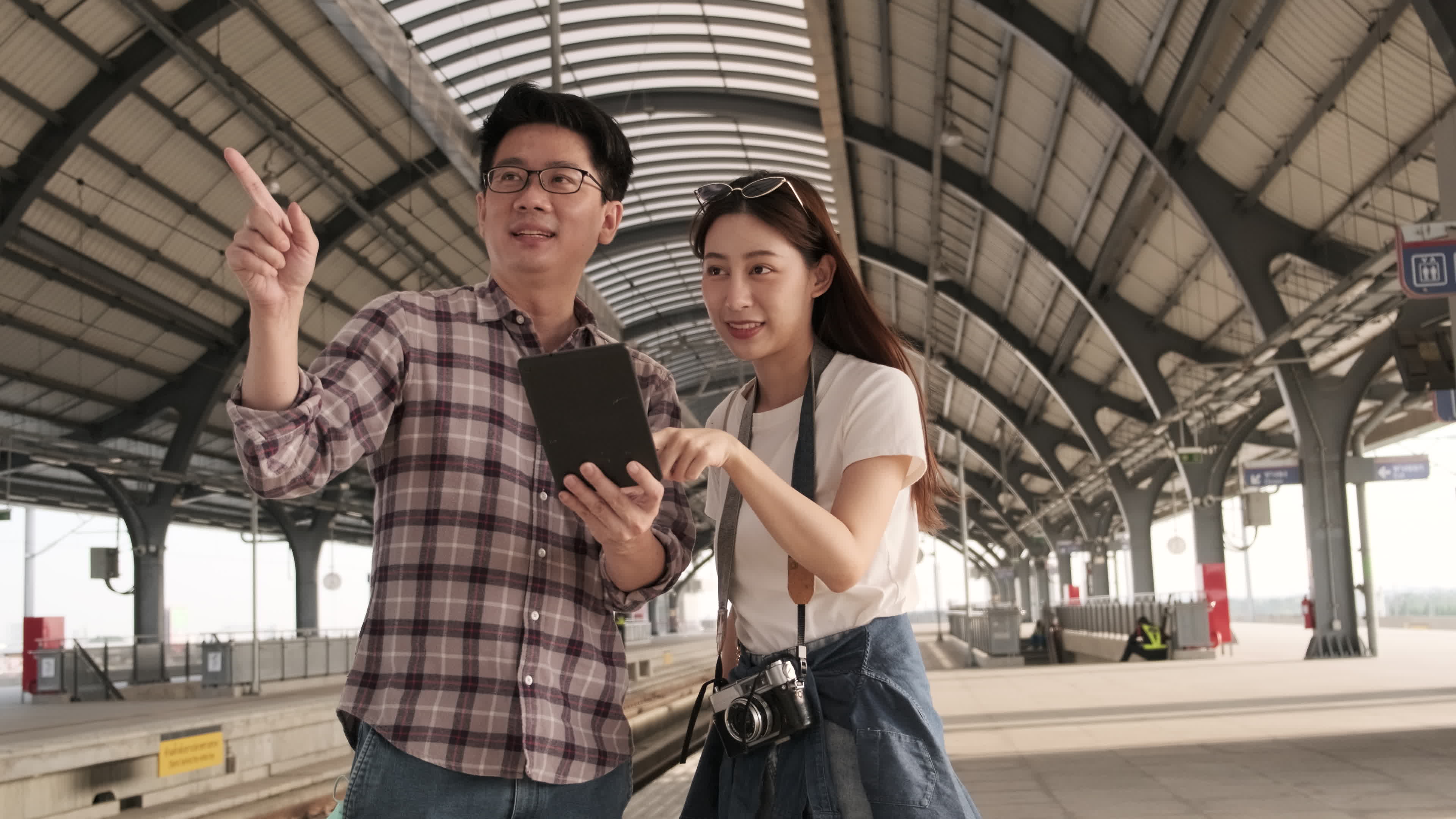 Young couple Asian tourists search information, find travel locations by tablet map at a train station junction in Thailand, passenger holiday trip lifestyle, casual transportation, journey vacation.