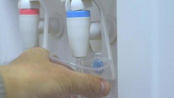 Male hand serving cold water of a water cooler in plastic cup. video