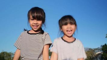 meninas de irmãos asiáticos felizes se abraçando no jardim de verão em um fundo de céu brilhante. retrato de menina sorridente no parque. video