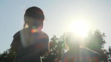 Silhouette glücklicher Schwestern, die ihre Hände heben und bei Sonnenuntergang in den Sommergarten springen. fröhliche Mädchen springen und spielen im Park. video