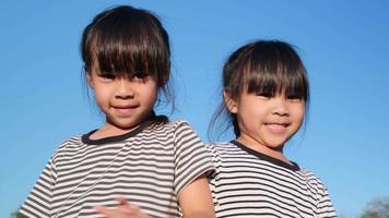 Happy Asian siblings girls hugging each other in the summer garden on a bright sky background. Portrait of smiling little girl in the park. video