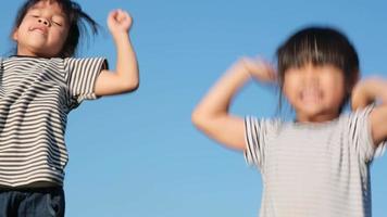 irmãs felizes levantando as mãos e pulando no jardim de verão ao pôr do sol. meninas alegres pulando e brincando no parque. video