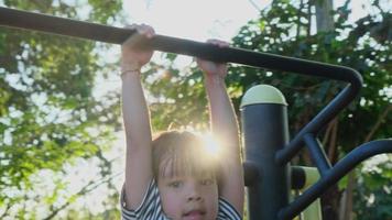 söt barn flicka hängande på träningsutrustning på utomhus lekplats. söt liten flicka som har kul i en park på en solig sommardag. video