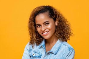 Close up portrait of happy young beautiful African American woman smiling while looking at camera in isolated studio yellow background photo