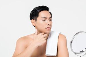 Shirtless young handsome Asian man looking at his face in the mirror  isolated on white background for skin care and beauty concepts photo