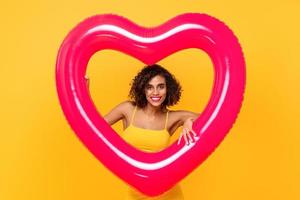 Happy smiling curly hair beautiful woman with colorful pink heart shape balloon isolated on yellow background photo