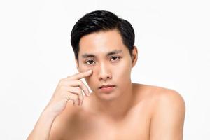 Handsome young Asian man touching under eye skin isolated on white background for beauty concepts
