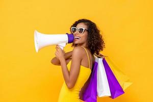 mujer hermosa feliz con bolsas de compras y megáfono sobre fondo amarillo colorido aislado para conceptos de venta y descuento foto