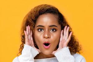 Fun close up portrait of surprised young beautiful African American woman  with hands cupped around opened mouth in isolated studio yellow background photo