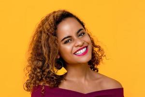 Close up portrait of happy young beautiful African American woman smiling while looking in front of camera in isolated studio yellow background photo