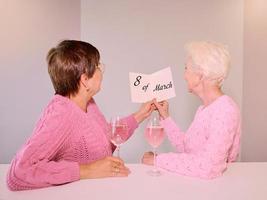 Two mature women drinking wine and giving a post card. Friendship, holidays, love, same-sex marriage concept photo