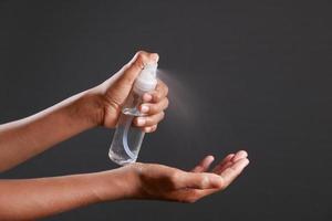 close up of young man hand using hand sanitizer spray isolated on black