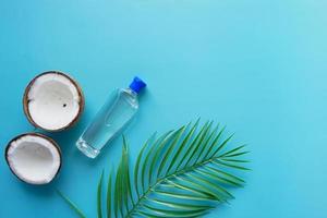 vista superior de una rodaja de coco fresco y una botella de aceite sobre fondo azul foto