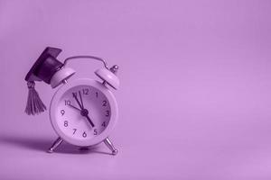 Yellow alarm clock with graduation cap on violet background closeup with copy space photo