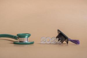 Graduation cap with stethoscope and numbers 2022 on beige background, closeup with copy space. Medical education concept. photo