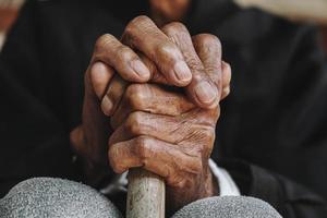 Asian old man sitting with his hands on a walking stick photo