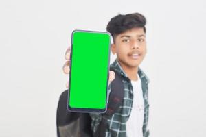 joven estudiante universitario indio que muestra la pantalla del teléfono inteligente con fondo blanco. foto