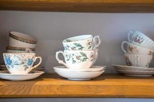 surtido de tazas de té con motivos florales y platillos en los estantes foto