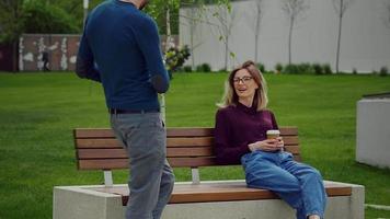 Handsome man brings lunch for colleague sitting on a bench in the park. video