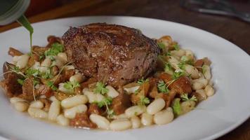 Man pouring delicious sauce on dish with beef steak and beans. video
