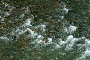 Turbulence in surface of water flowing through rocky pebble photo