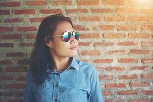 retrato de un hermoso hipster sonriente con gafas de sol contra una pared de ladrillo rojo. foto