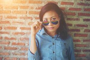 Portrait of a beautiful smiling hipster wearing sunglasses against a red brick wall. photo