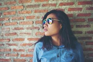 retrato de un hermoso hipster sonriente con gafas de sol contra una pared de ladrillo rojo. foto