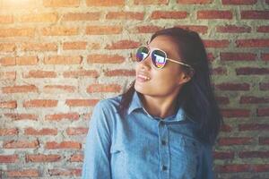 Portrait of a beautiful smiling hipster wearing sunglasses against a red brick wall. photo