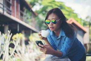 joven hipster mirando su teléfono mientras sostenía una taza de café por la mañana y sonreía. relajante concepto de vacaciones. foto