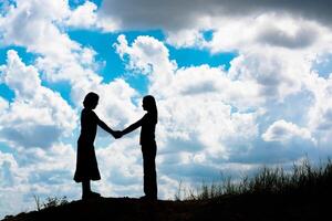 silhouette of two girls facing each other hold hands together photo