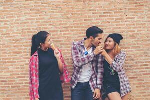 Portrait of a group of friends eating ice-cream in front of brown brick wall. photo