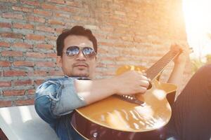 hombres hipster guapos practican para tocar la guitarra mientras él disfruta de la relajación con la naturaleza alrededor. foto