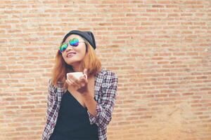 Cheerful woman in the street drinking morning coffee against brick wall. photo