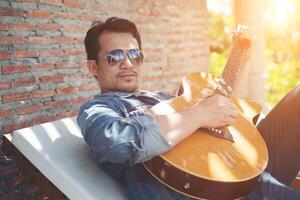 Handsome hipster men practice to play guitar while he is enjoying the relaxing with nature around. photo
