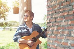 Handsome man leaning against a brick wall while playing the guitar. photo