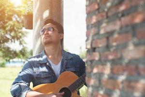 Handsome man leaning against a brick wall while playing the guitar. photo