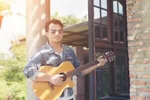 Handsome man leaning against a brick wall while playing the guitar. photo