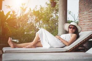 Portrait of charming woman relaxing on the deck chair outdoors with hat and glasses. photo