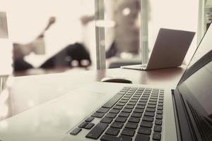 business documents on office table with smart phone and laptop and two colleagues discussing data in the background photo