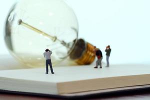 Creative idea concept - miniature photographer with vintage light bulb on open paper notebook photo